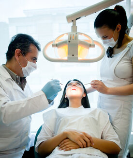 woman getting dental work done in chair, male and female dentists next to her